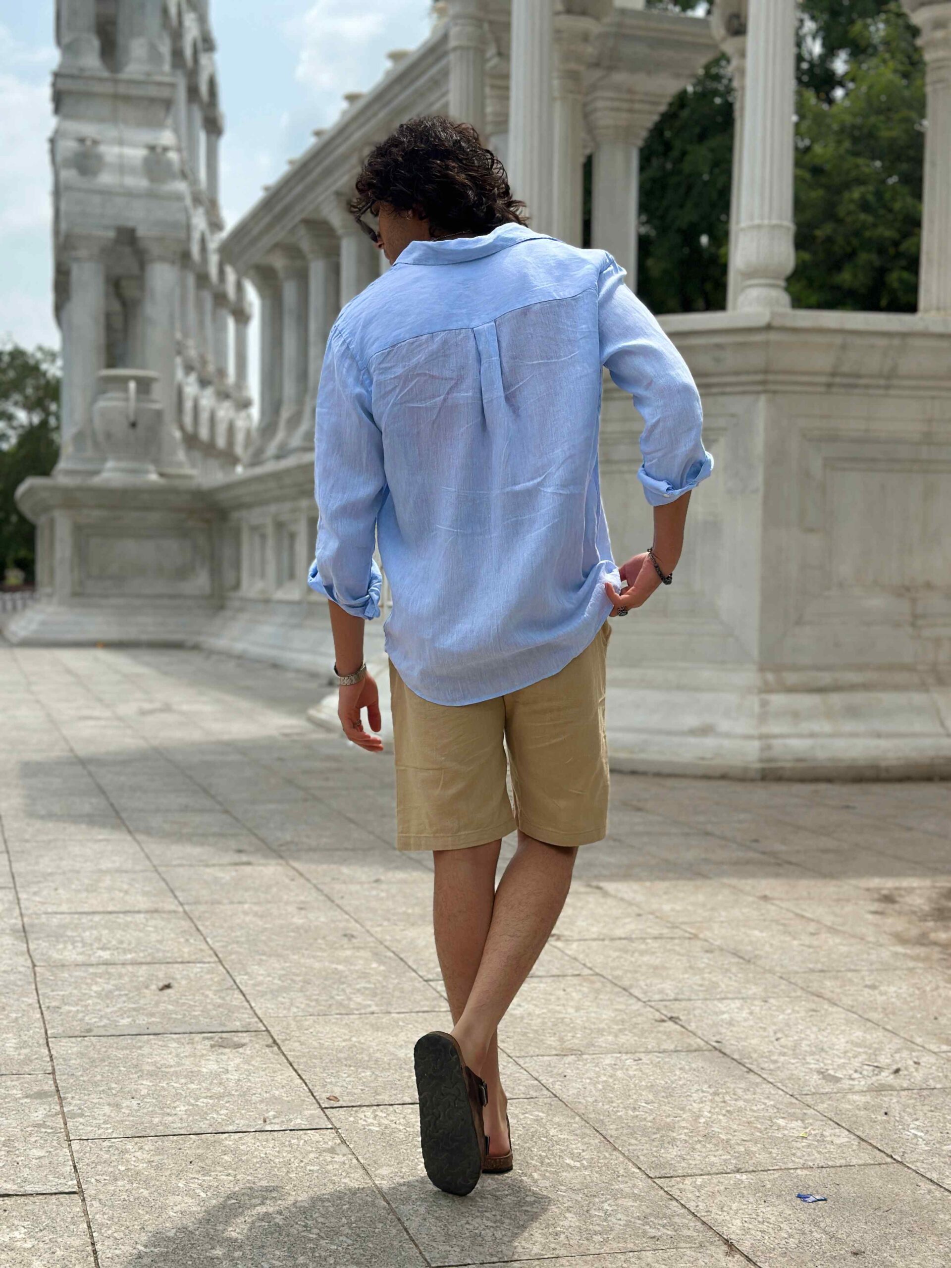 Man from behind, showing the full length and fit of the cream linen shorts.