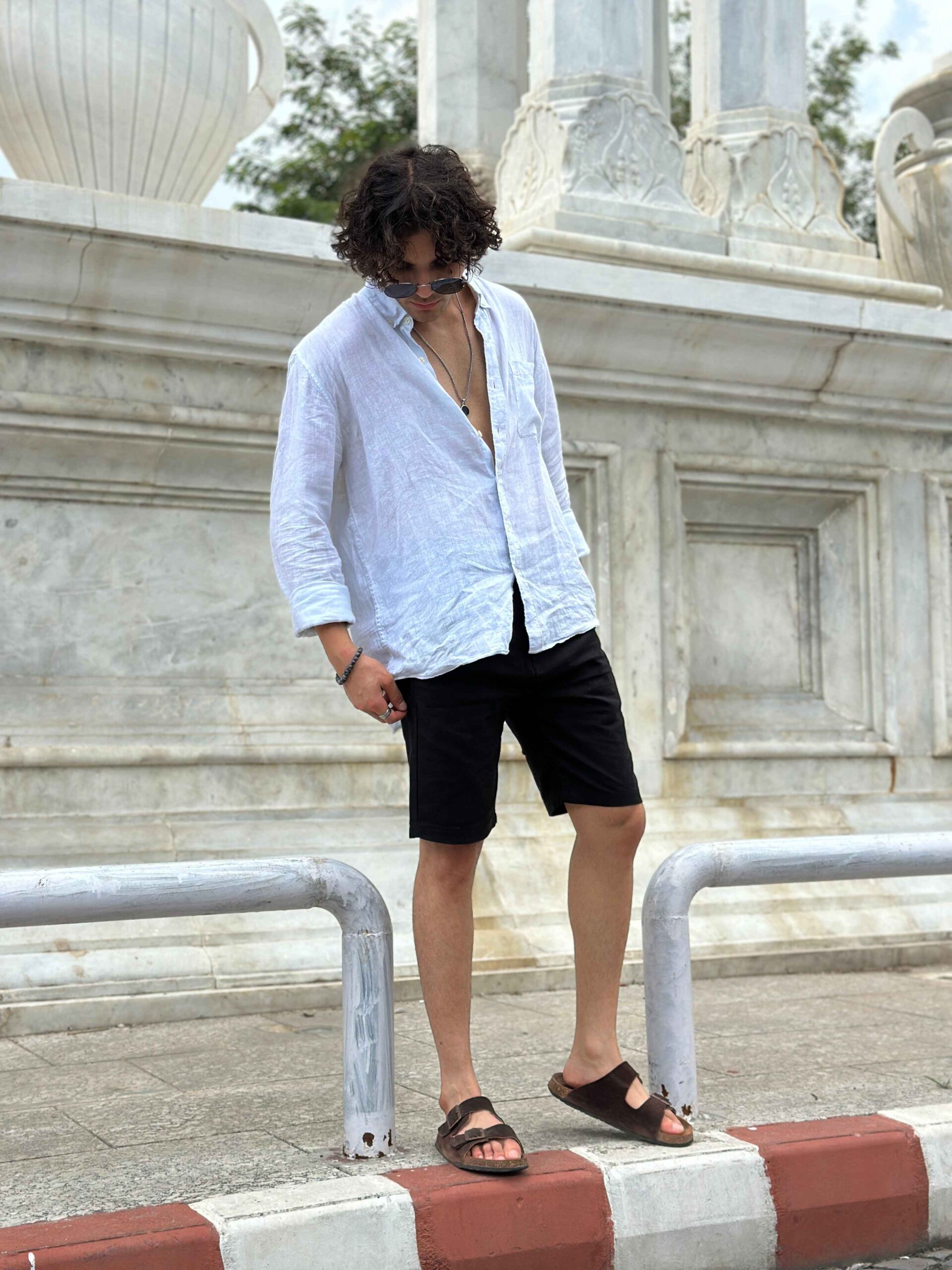 Man in black linen shorts and a white shirt, showcasing a stylish, relaxed fit