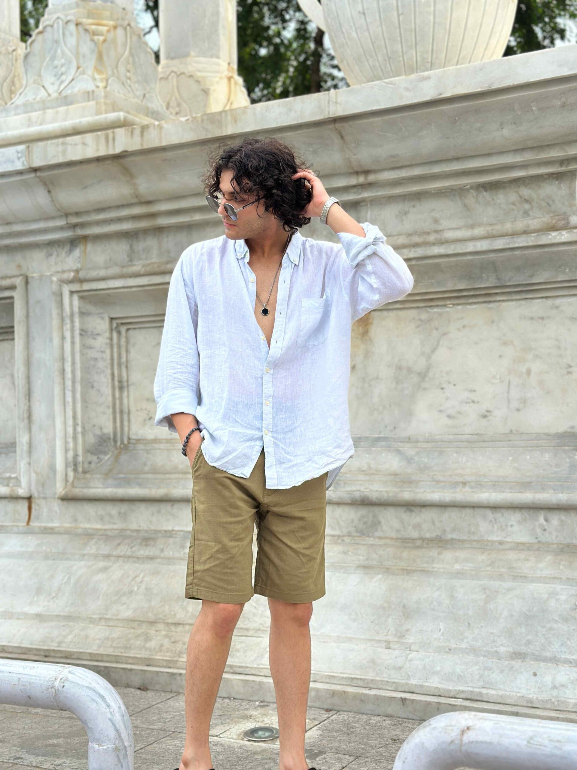 Man in trendy khaki linen shorts, paired with a white linen shirt and sunglasses, posing for a stylish summer photo.