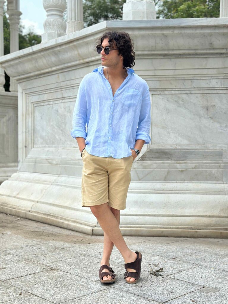 Man models cream linen shorts with a light blue linen shirt and sunglasses.