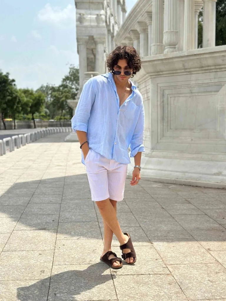 Men's white linen shorts, styled with a light blue button-up shirt and brown sandals, perfect for a fashionable and comfortable summer look.
